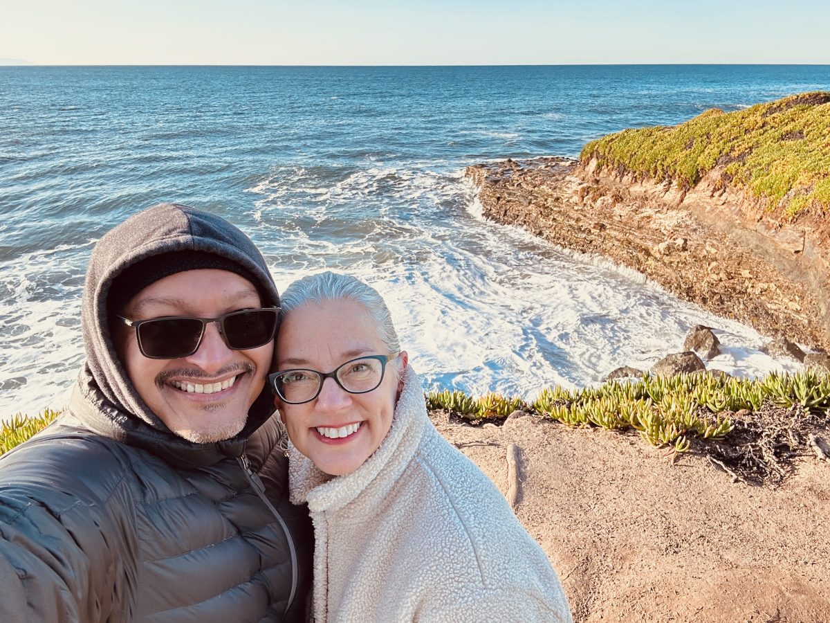 A man and woman smiling with the ocean and cliff in the background 
