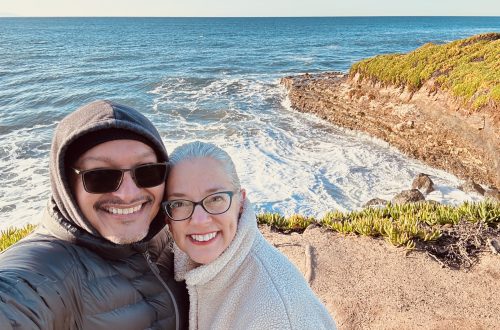A man and woman smiling with the ocean and cliff in the background
