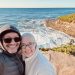 A man and woman smiling with the ocean and cliff in the background